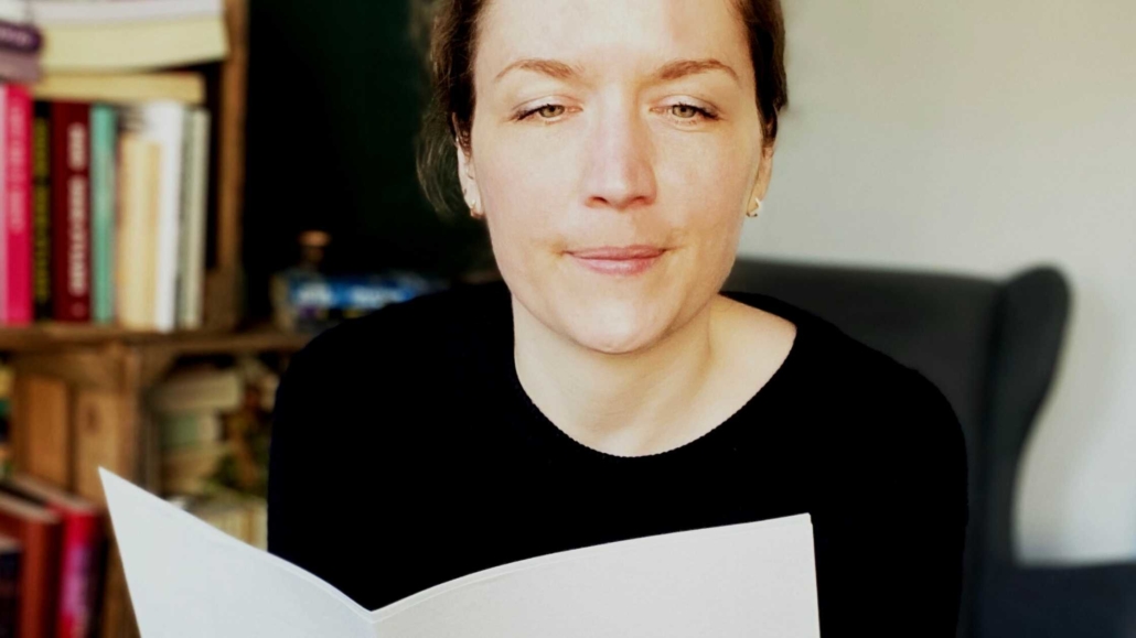 Svenja Hirsch sitzt vorgelehnt auf einem Hocker und liest in ein paar ausgedruckten Seiten